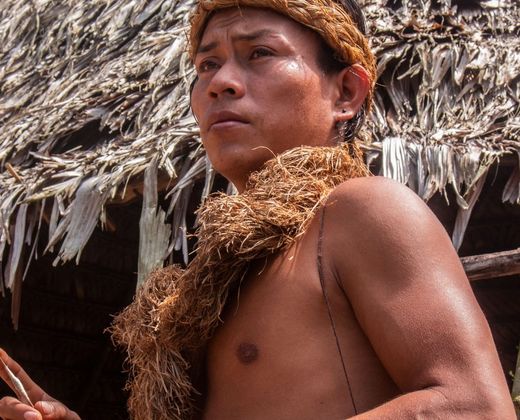 Homem indígena diante de uma moradia tradicional