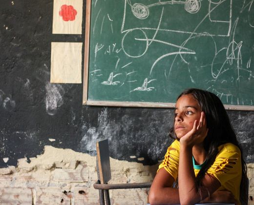 Aluna pensativa em sala de aula com lousa ao fundo