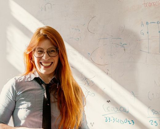 Professora sorrindo em frente ao quadro-negro