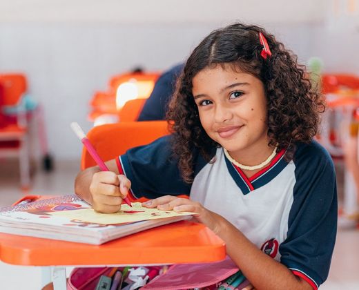 Menina sorridente fazendo atividade escolar em carteira