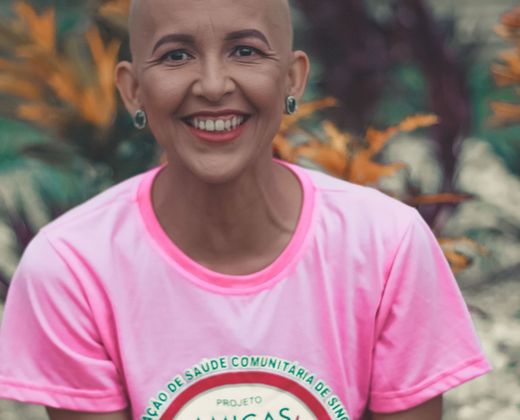 Mulher em tratamento oncológico sorrindo, com camiseta de um projeto de saúde comunitária