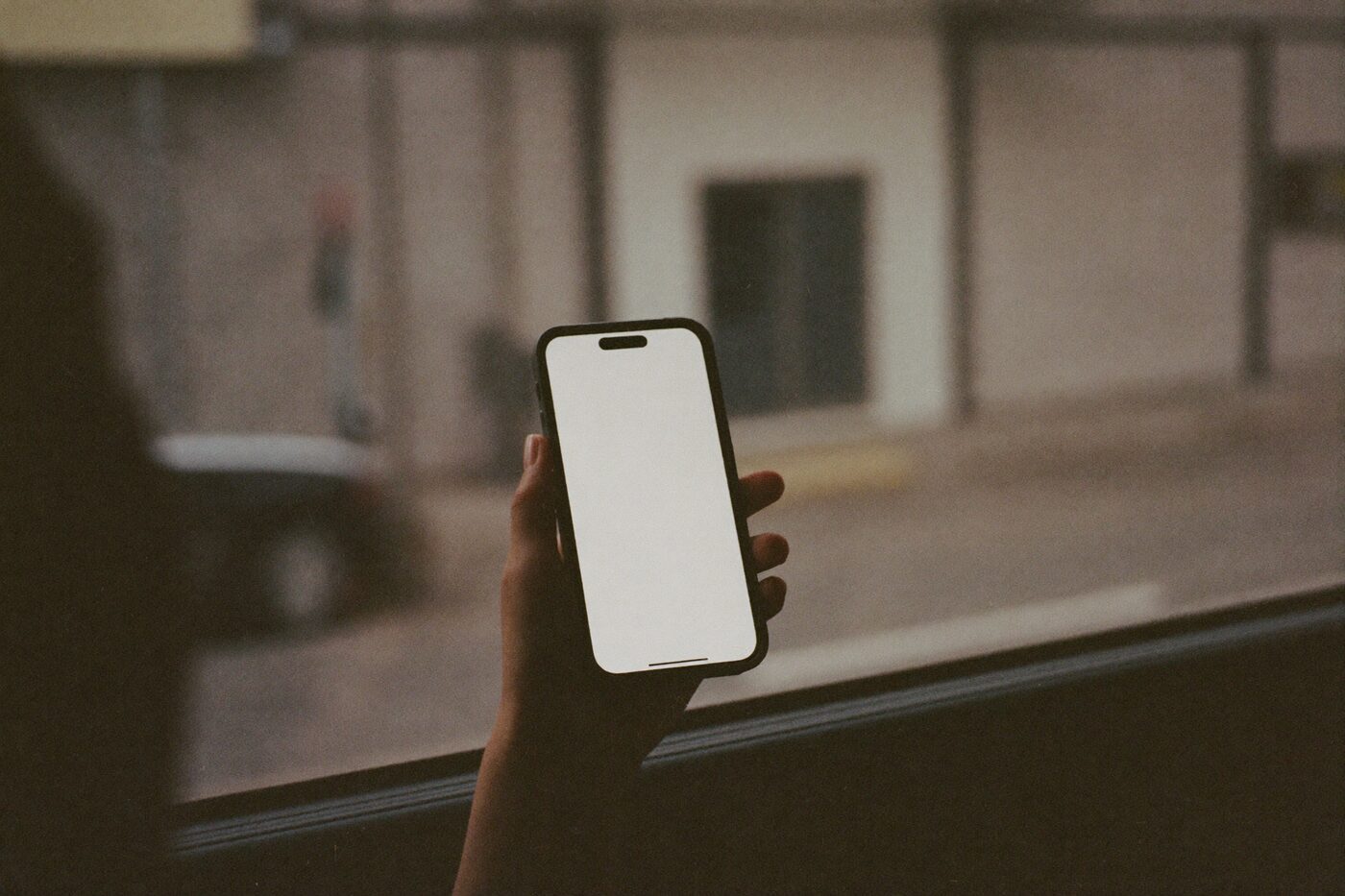 Mão segurando um celular dentro de um ônibus, com a rua de uma cidade brasileira desfocada pela janela.