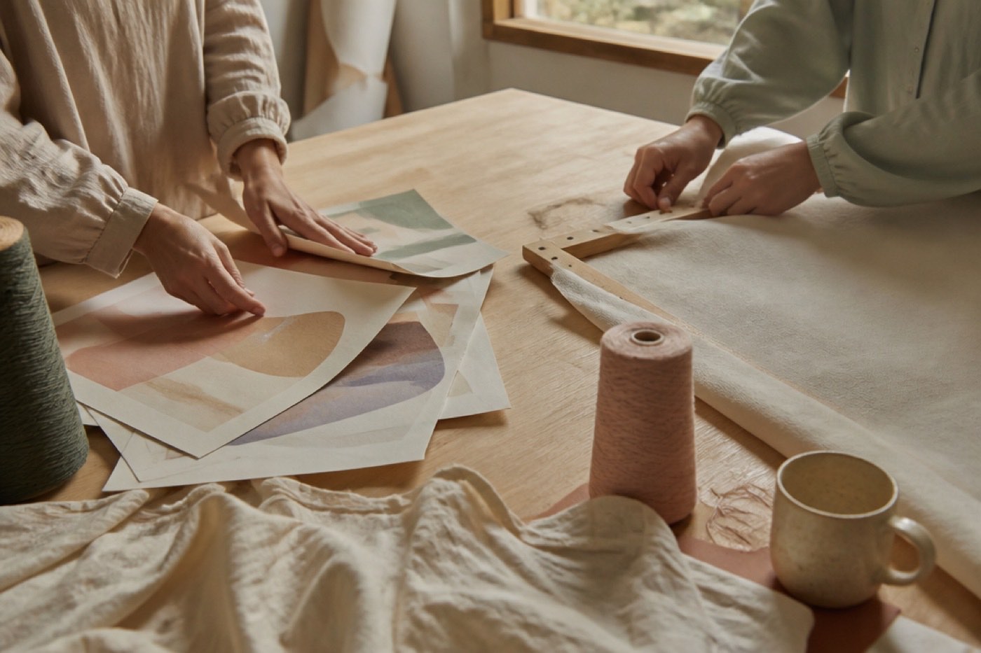 Mãos organizando materiais gráficos e tecido sobre uma mesa de trabalho de um projeto cultural
