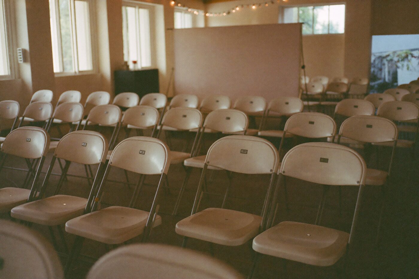 Fileiras de cadeiras montadas em um salão comunitário antes de um evento beneficente, com luz de fim de tarde entrando pelas janelas.