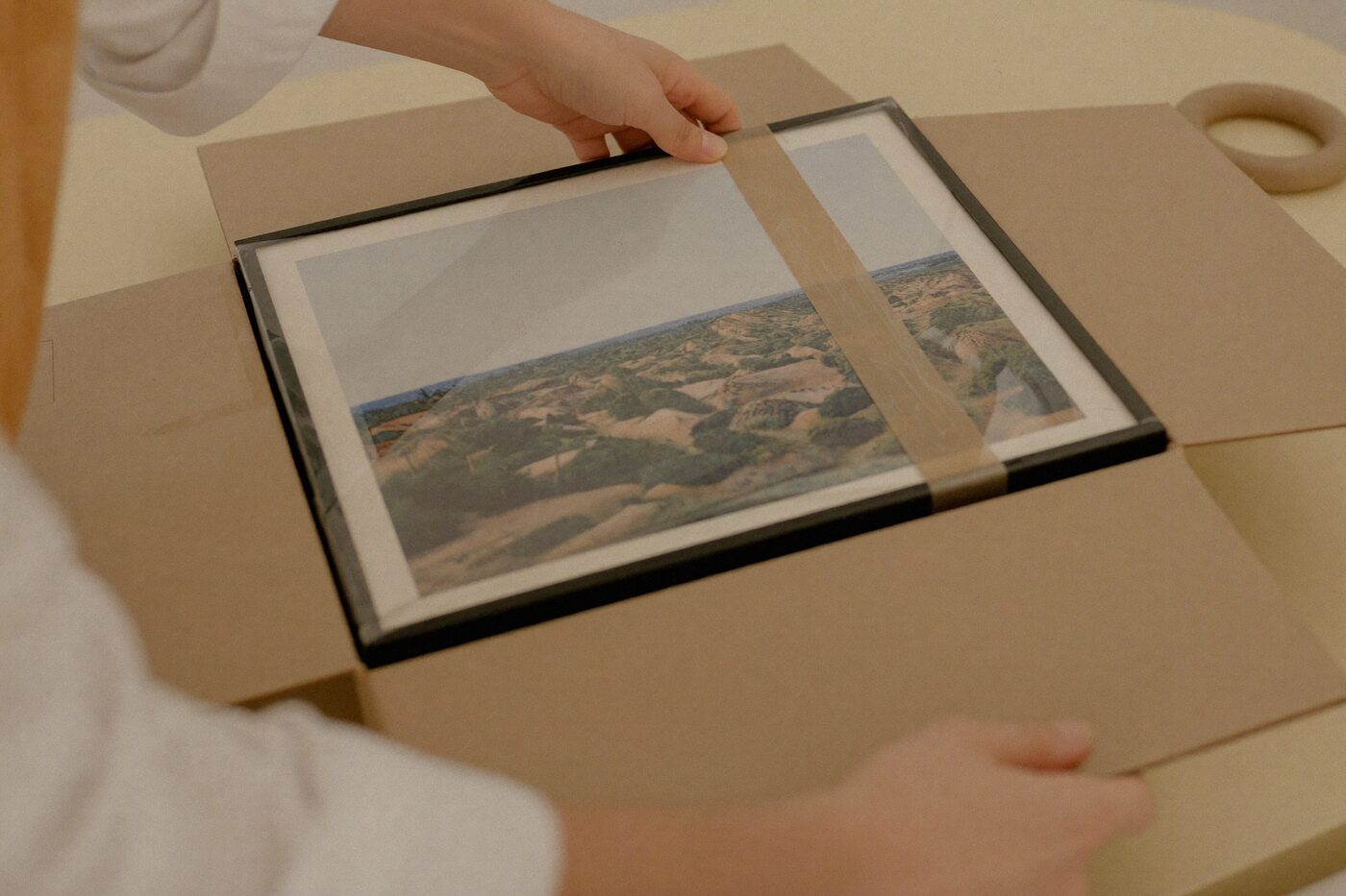 Mãos embalando um quadro emoldurado dentro de uma caixa de papelão para envio ao arrematante.