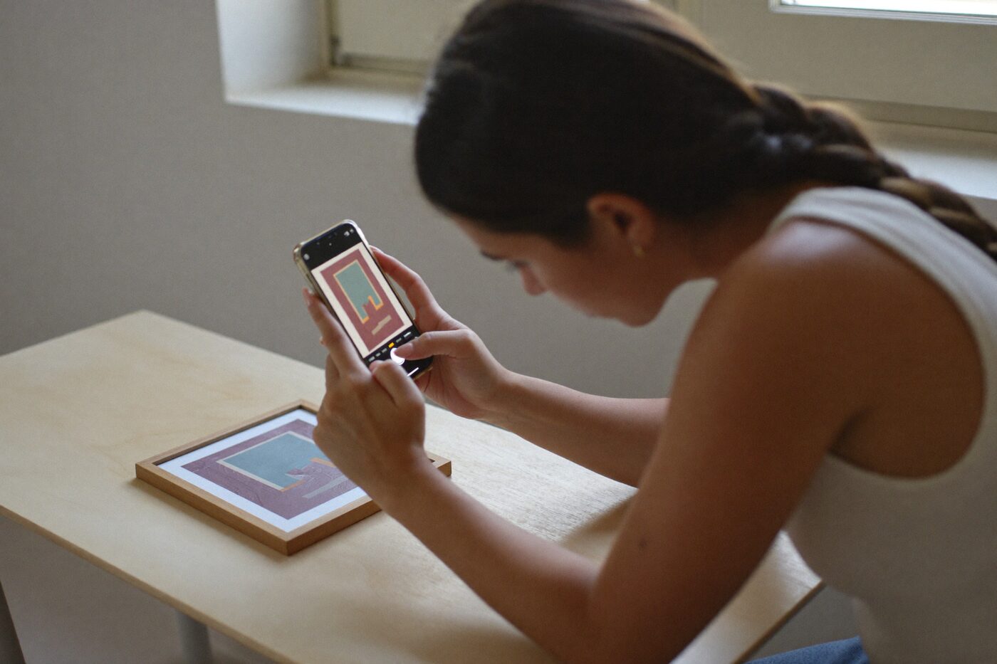 Pessoa fotografando com o celular um quadro emoldurado apoiado na mesa, para montar a galeria do leilão.