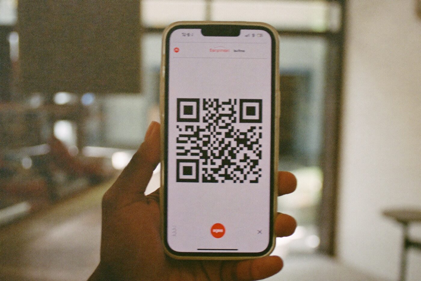 Mão segurando um celular que exibe um código QR, em um balcão com luz natural.